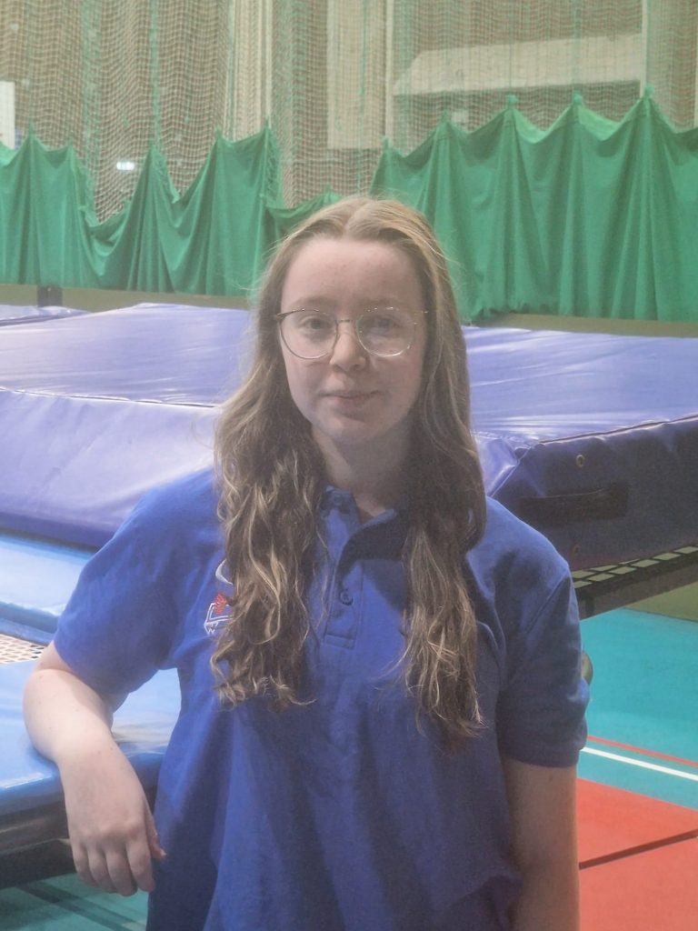 image of abi grundy in a blue Club polo shirt standing in front of a trampoline